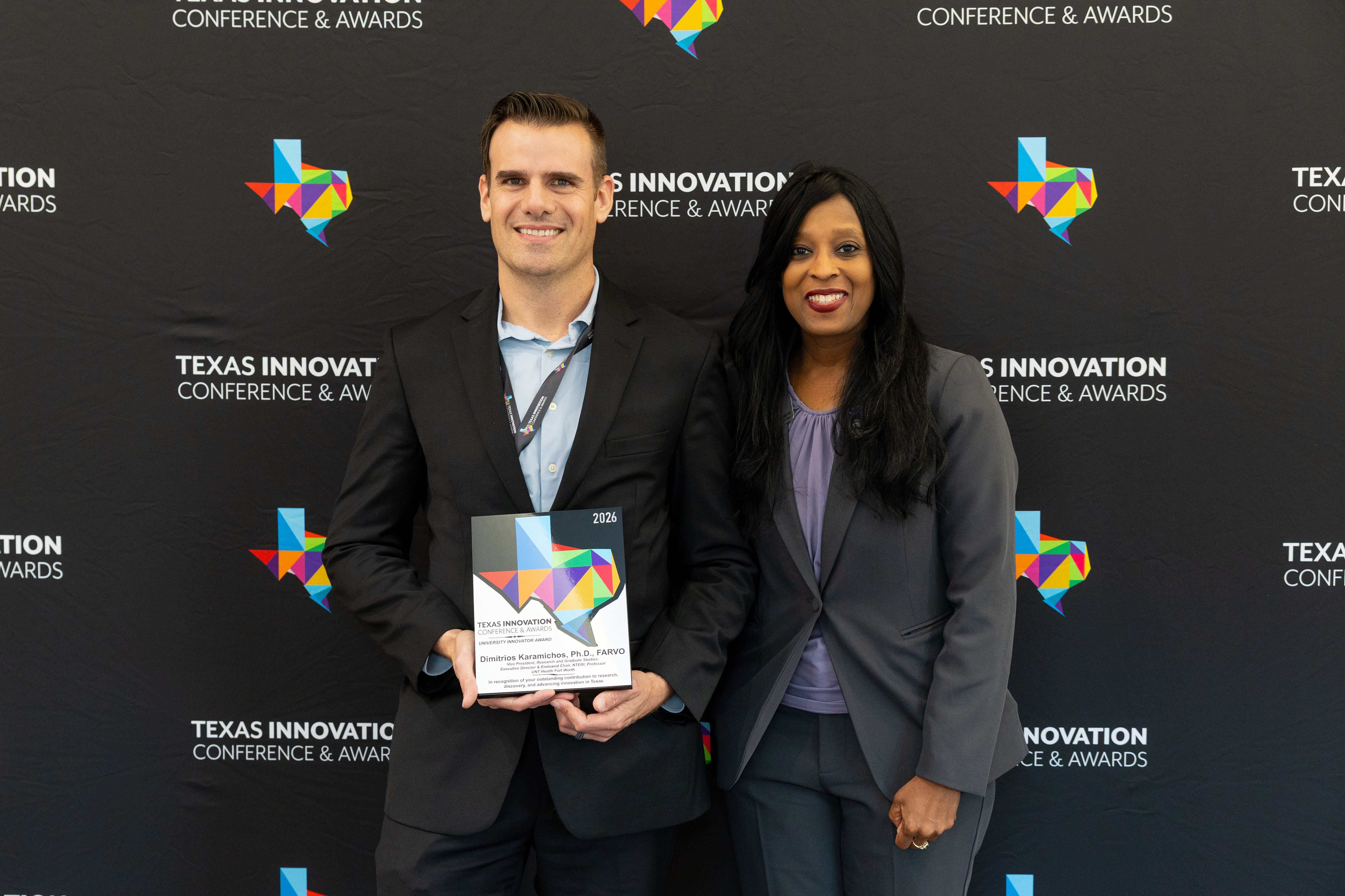 Photo of UNT Health's Dr. Dimitrios Karamichos, PhD, holds his 2026 University Innovator Award plaque at the Texas Innovation Conference & Awards ceremony, posing alongside a presenter in front of the event step-and-repeat backdrop.