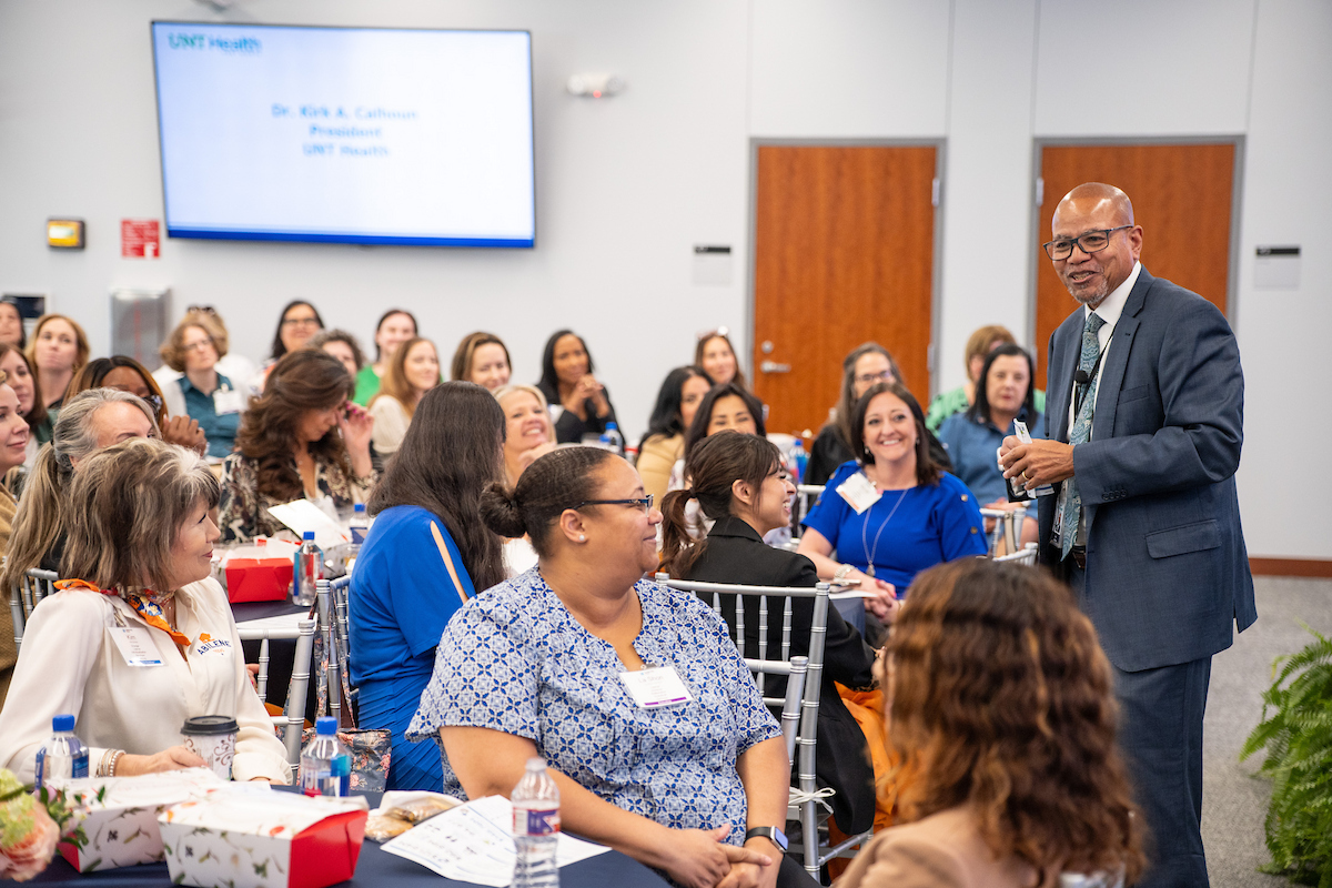 Photo of UNT Health's Dr. Kirk Calhoun stands among the seated female visitors as he welcomes them to the 2026 Leadership Texas event.