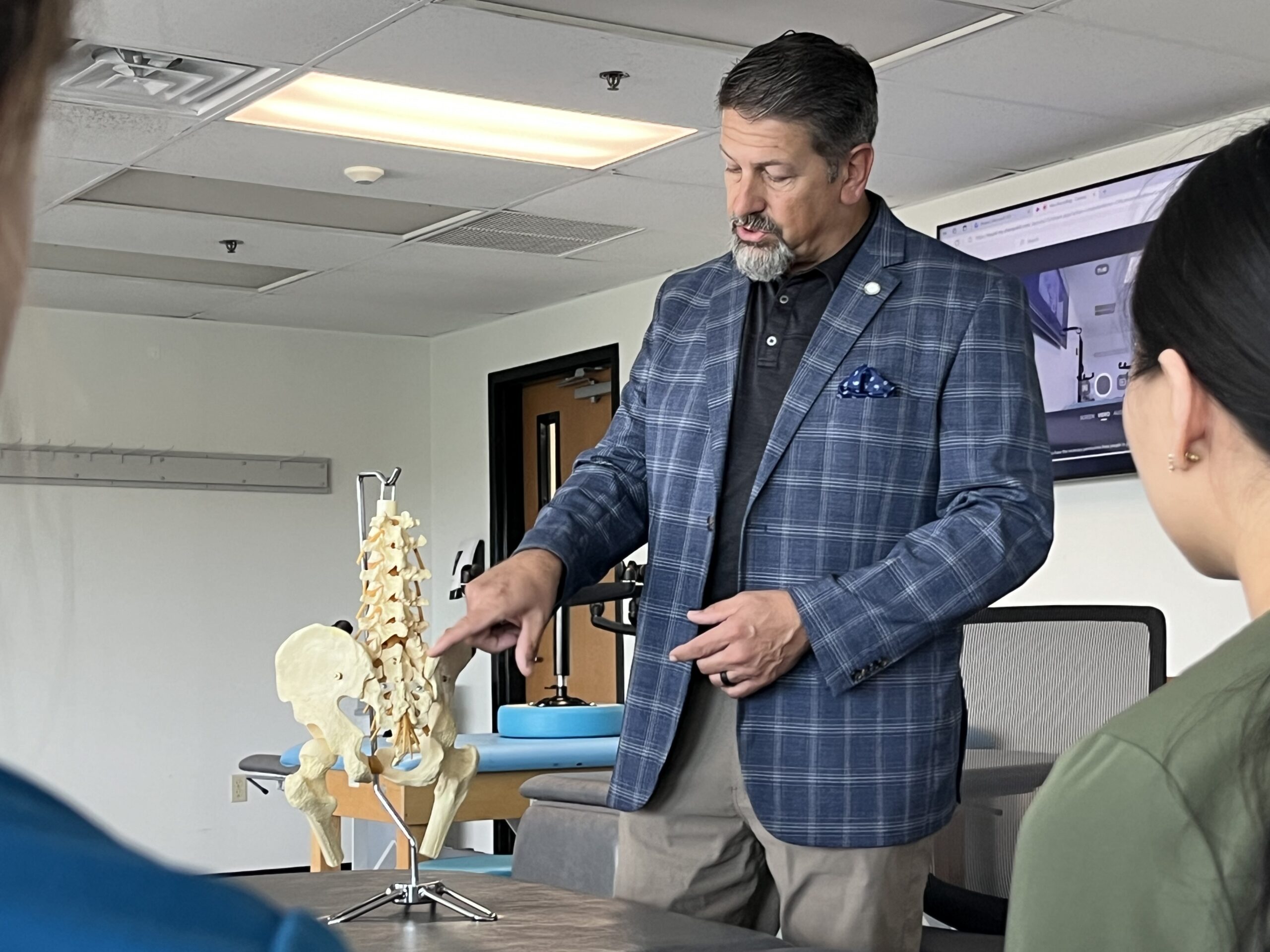 Photo of UNTHSC. TCOM's Dr. David Mason in a classroom pointing to a life-size model skeleton of replicating a human hip and tale bone on a stand