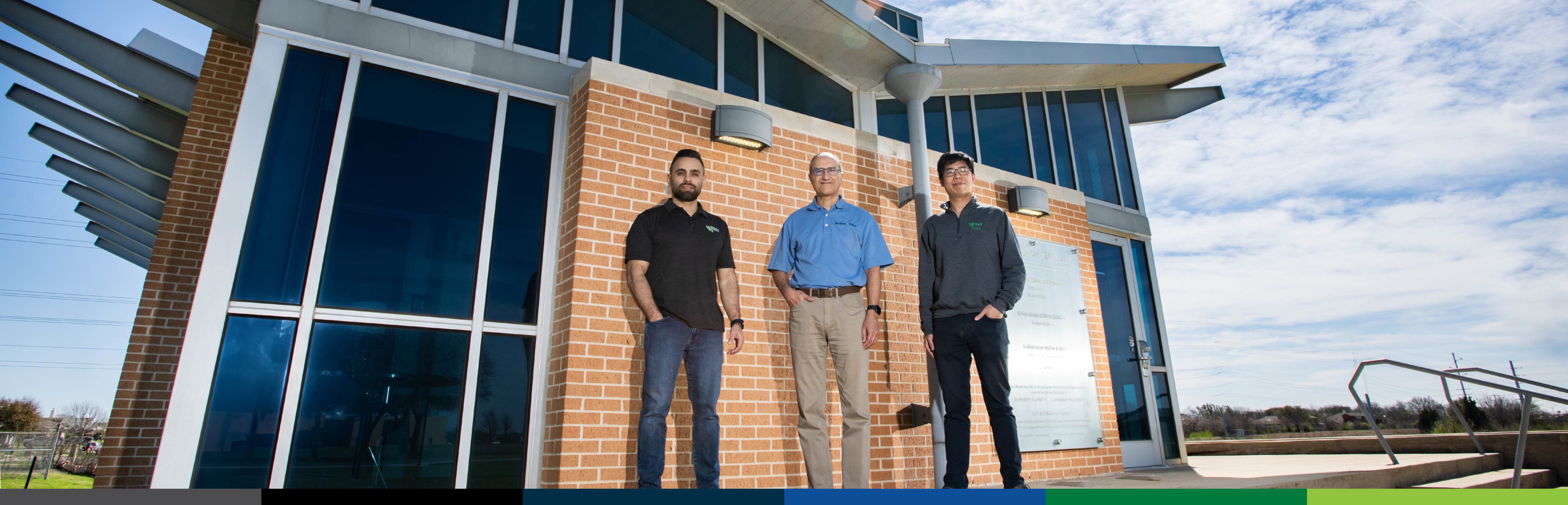 Photo of 3 UNT researchers standing in front of the Zero Energy Research Lab building at the University of North Texas
