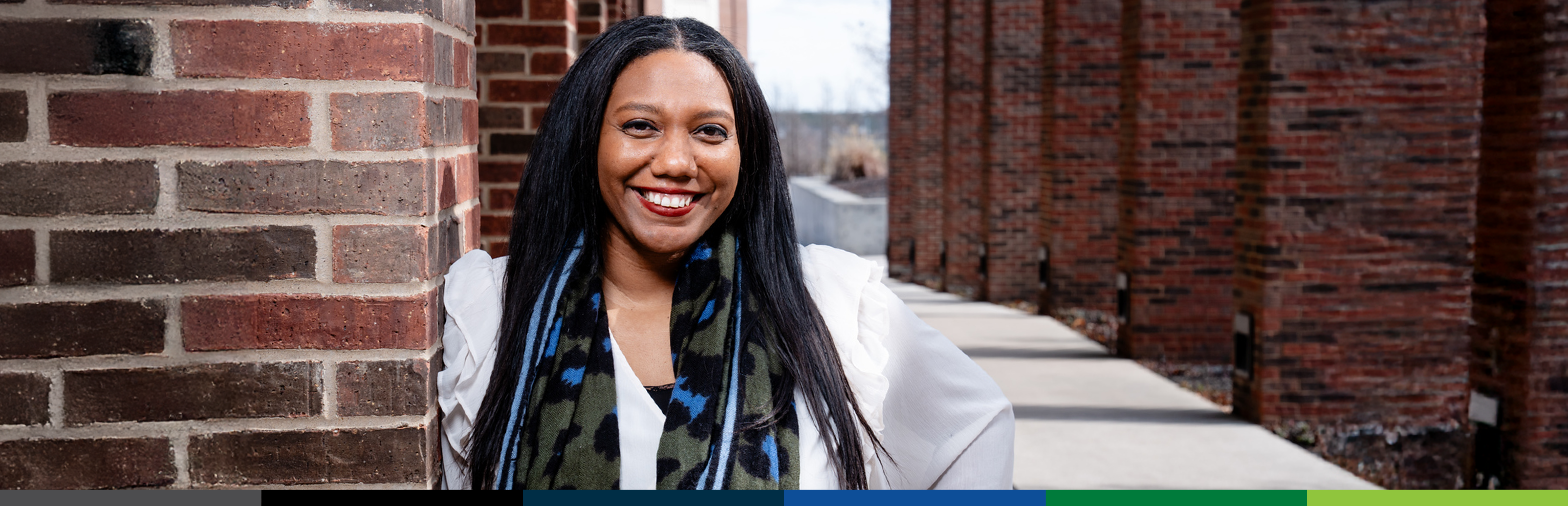 Standing outside leaning against a brick wall is Jessica Alvarez, UNT Dallas Asst. Dean for Student Success in Health Professions 