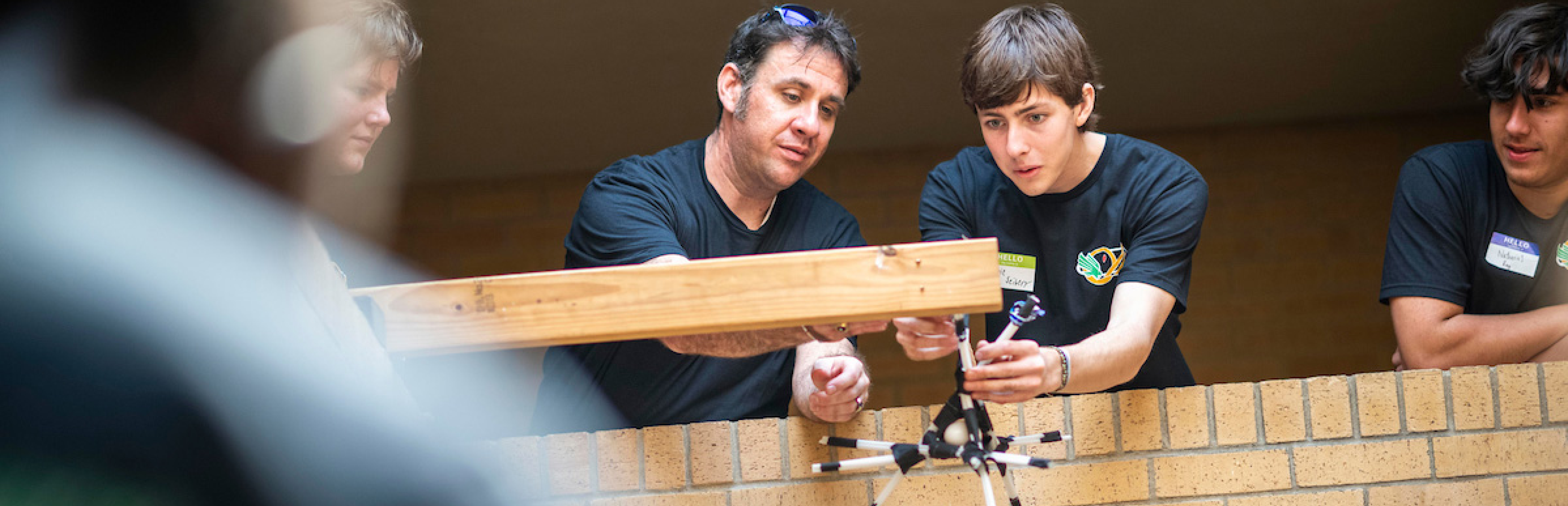 Photo of UNT faculty helping students learn hands-on about physics-based formulas being applied to testing and building items such as bridges