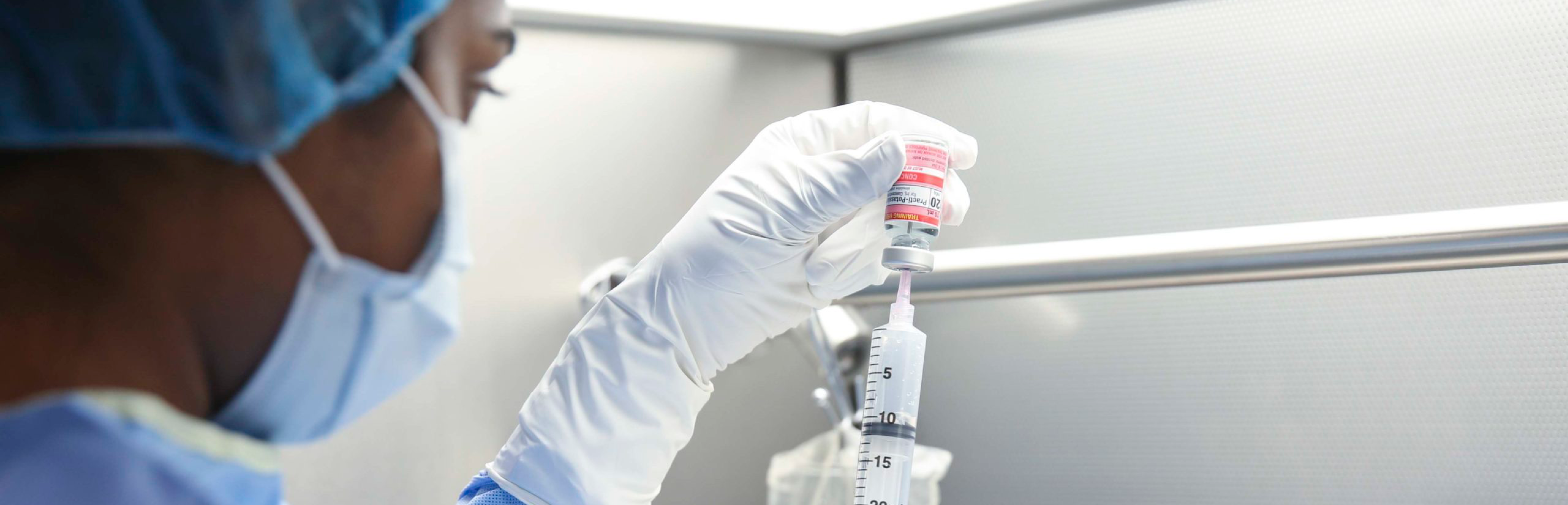 A photo of a gloved healthcare worker drawing medication from a vial into a syringe in a laboratory setting.